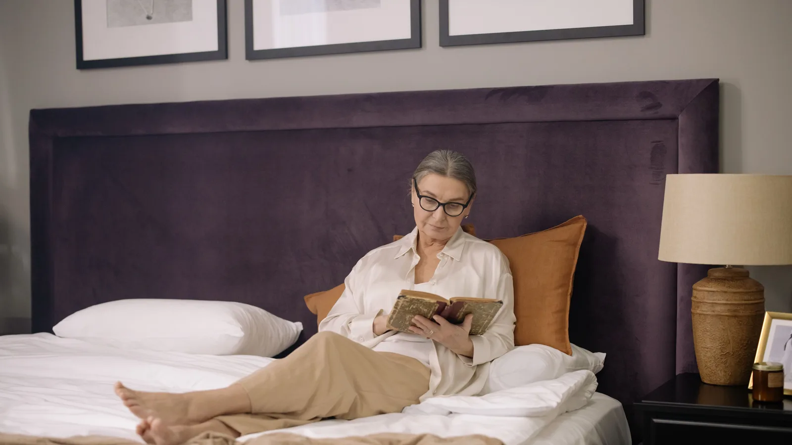 Lecture au lit à la lumière d'une petite lampe orientée sur la page, le reste de la chambre dans la pénombre.